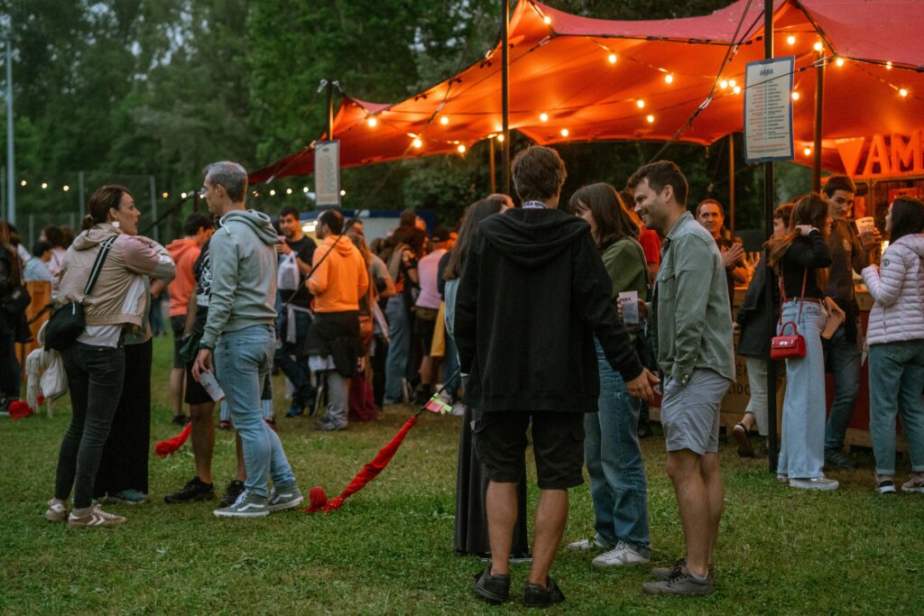A lively outdoor festival with people socializing under a tent with string lights.