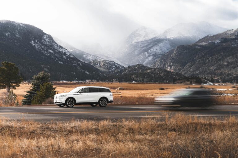 A white SUV drives along a scenic road in Colorado Springs, surrounded by stunning mountain views.